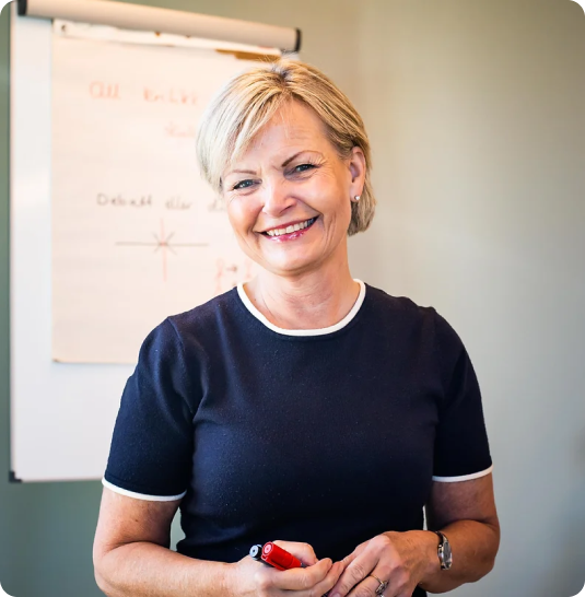 smilende dame foran en tavle, blondt hår og sort Tskjorte